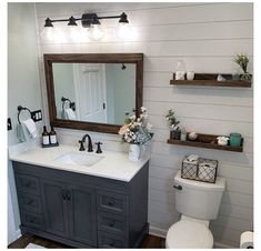 a white toilet sitting next to a sink in a bathroom under two wooden shelves filled with flowers