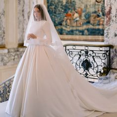 a woman in a white wedding dress and veil standing next to a wall with paintings on it