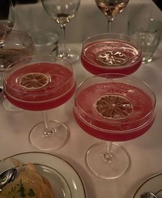 three glasses filled with different types of drinks on top of a white cloth covered table