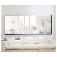 a living room with white furniture and a large mirror on the wall above it's couch