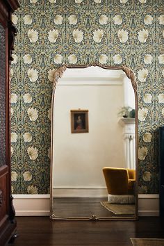 a large mirror sitting on top of a wooden floor next to a wallpapered wall