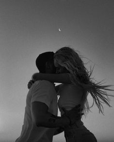 a man and woman embracing each other on the beach at sunset with moon in background