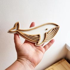 a hand holding a wooden cutout of a whale in white and tan colors with gold accents