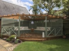 a wooden deck with benches and chairs under a pergolated roof in a backyard