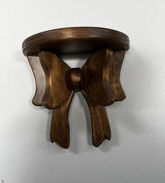 a wooden shelf with a bow on it's top hanging from the wall in front of a white wall