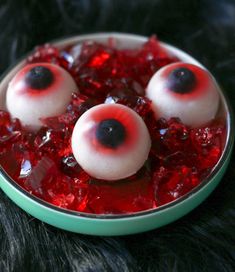 three fake eyes are in a bowl of red crushed ice with blackberries on top