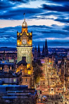 a clock tower in the middle of a city at night with lights on it's sides