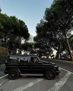 a black suv parked on the side of a road in front of trees and bushes