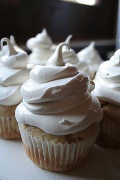 several cupcakes with white frosting sitting on a table