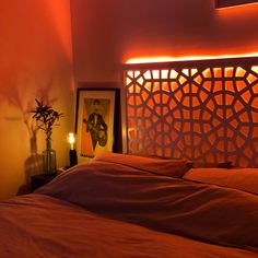 a bed with an orange comforter next to a framed photograph and a lamp on the wall