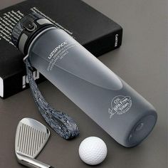 a golf ball, driver's club and water bottle sitting on a table next to a book