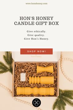 the honey candle gift box is open and has two candles in it, with pine branches around