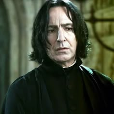 a man with long black hair wearing a dark outfit and looking off to the side