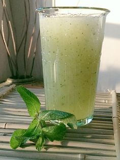 a tall glass filled with green liquid sitting on top of a wooden table next to a plant