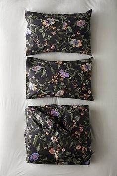 two pillows on top of a bed with floral print and white sheets in the background