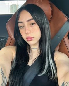 a woman with long black hair sitting in the back seat of a car and looking at the camera