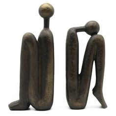 two metal sculptures sitting next to each other on a white surface with one standing and the other seated