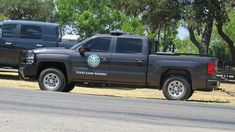 two black trucks are parked on the side of the road in front of some trees