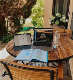 an open laptop computer sitting on top of a wooden table next to a vase with flowers