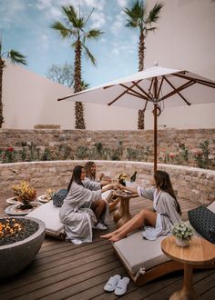 two women in robes are sitting on a wooden deck with an umbrella over the table