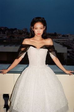 a woman in a white dress standing on a ledge with her arms out and hands behind her back