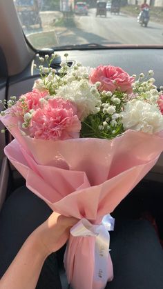 a bouquet of pink and white flowers in the back seat of a car with someone's hand holding it