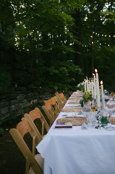 a long table is set up with candles and place settings for an outdoor dinner party