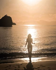 a woman is walking on the beach at sunset