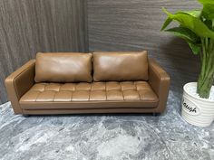 a brown leather couch next to a potted plant on a marble flooring surface