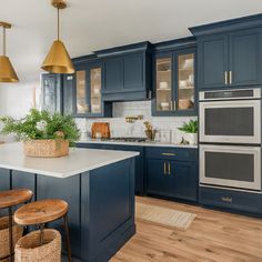 a large kitchen with blue cabinets and white counter tops, gold pendant lights over the island