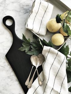 a black cutting board topped with fruit next to a white towel and two silver spoons