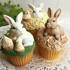 three cupcakes decorated with bunnies and bunny figurines on a doily