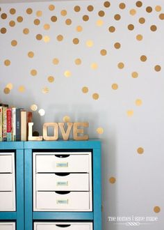 a blue dresser with gold polka dot decals on the wall next to bookshelves