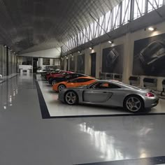 there are many different cars parked in this garage together on the floor and one is orange