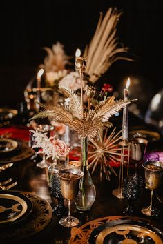 a table topped with lots of plates covered in gold and black decorating items next to candles