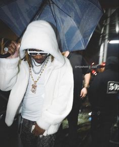 a man in a white jacket and sunglasses holding an umbrella over his head while standing next to other people