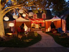 tents set up in front of a house with lights strung from the trees and around them