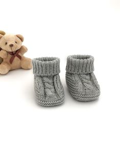 a teddy bear sitting next to two knitted baby booties on a white background