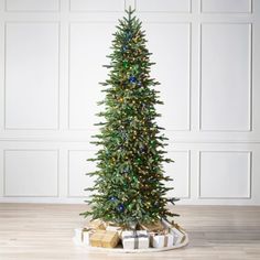 a christmas tree with presents under it on a wooden floor in front of a white wall