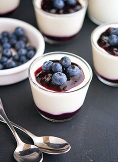 blueberries and yogurt are in small bowls with spoons on the table