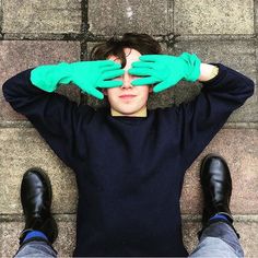 a person with green gloves covering their eyes and hands over their head, sitting on the ground