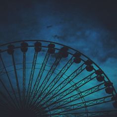 a large ferris wheel sitting under a cloudy blue sky at night with the moon in the distance