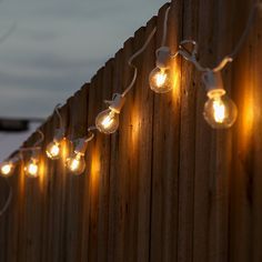 some lights are hanging on the side of a wooden fence with string lights attached to it