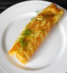 an omelet on a white plate with green garnish and sprigs