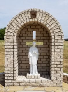 a statue of a person holding a cross in front of a brick wall with a stone arch