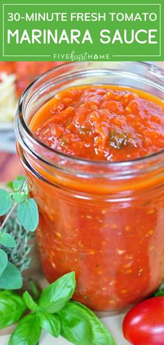 a jar filled with marinara sauce next to tomatoes and basil