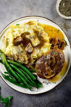 a plate with mashed potatoes, green beans and mushrooms next to some seasoning