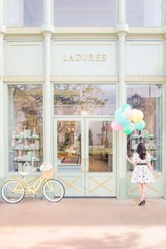 a woman is holding balloons in front of a store with a bicycle parked next to it