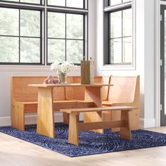 a wooden table and bench sitting in front of two windows with blue rug on the floor