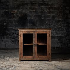 an old wooden cabinet with glass doors in front of a brick wall and stone floor